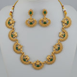 Gold jewelry set with green stones held in a hand against a natural background