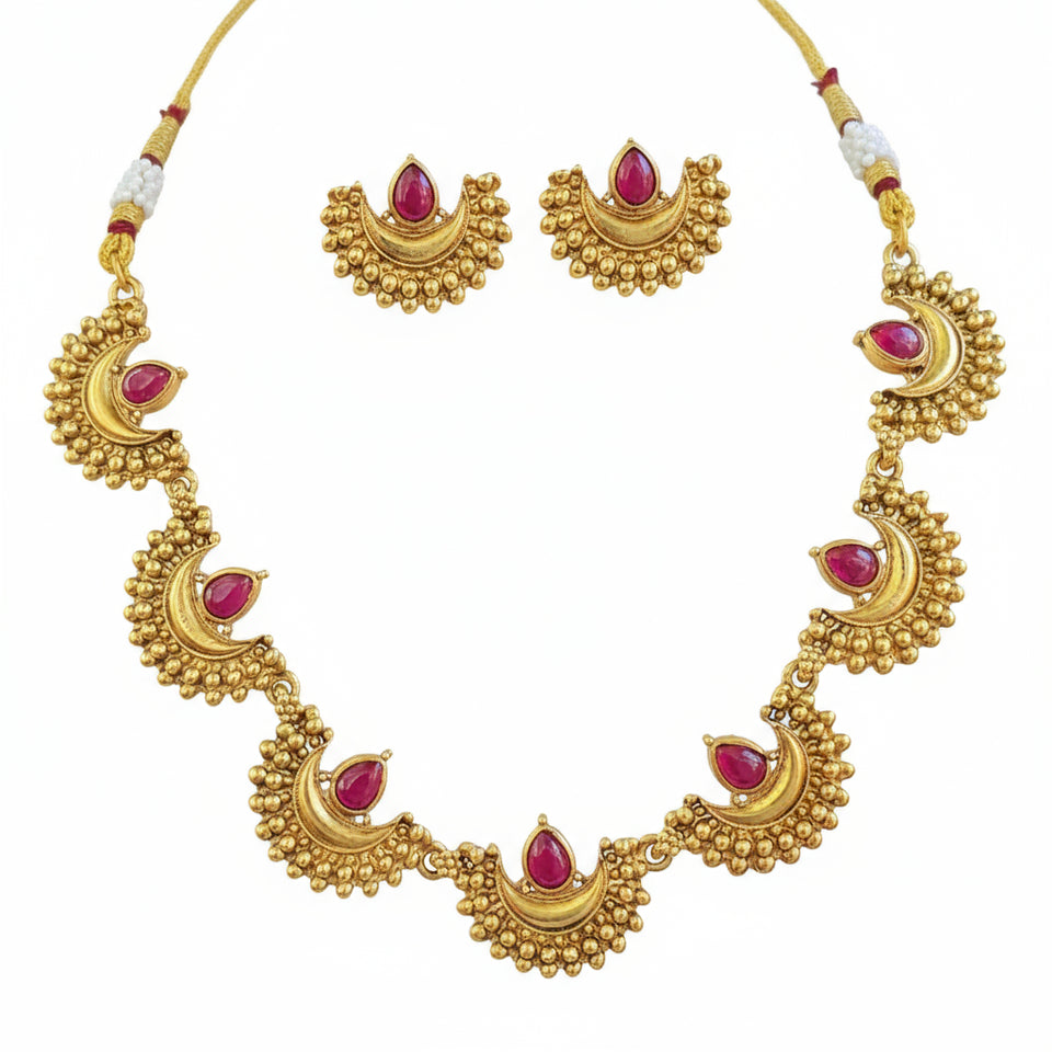 Gold necklace with red gemstones held in a hand against a blurred natural background