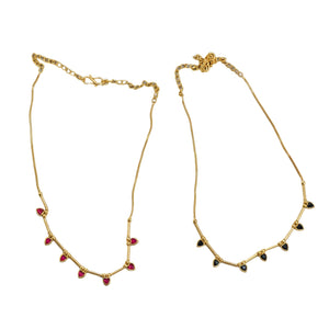 Two gold necklaces with red and black beads on a white fabric background with a green leaf.