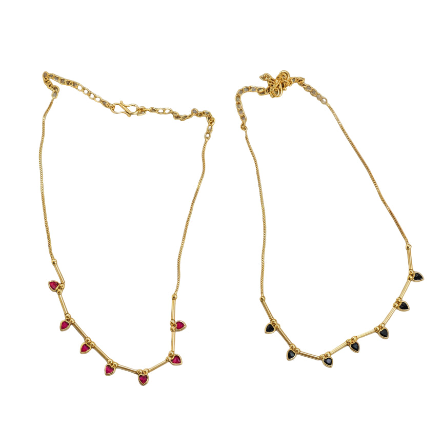 Two gold necklaces with red and black beads on a white fabric background with a green leaf.