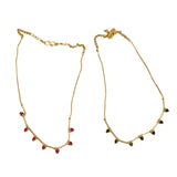 Two gold necklaces with red and black beads on a white fabric background with a green leaf.