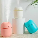 Three small humidifiers in white, pink, and blue on a textured surface with a light background.